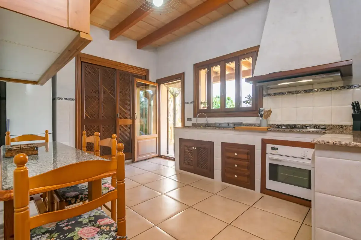 A kitchen and dining area with wooden cabinetry, a tiled floor, and exposed ceiling beams.