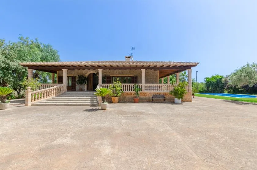 A single-story house with a covered porch and broad paved courtyard.