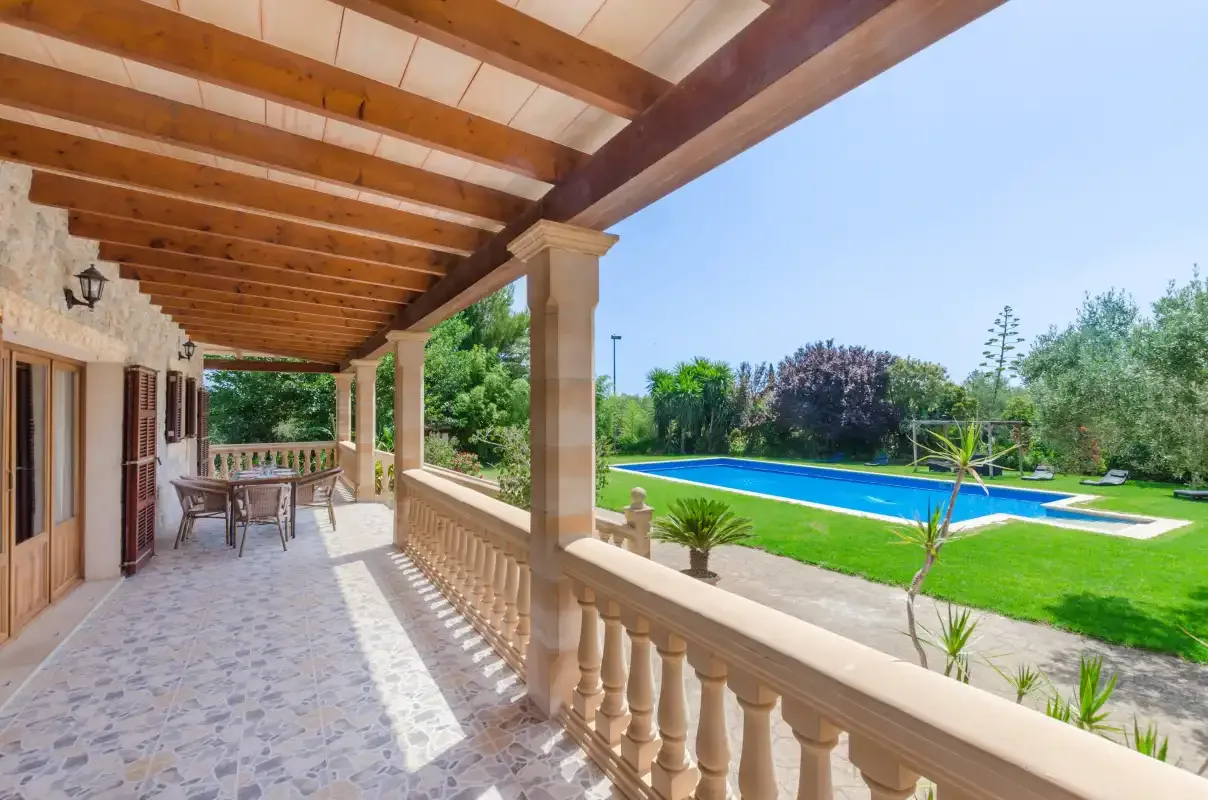 A covered patio overlooks a swimming pool and lawn.