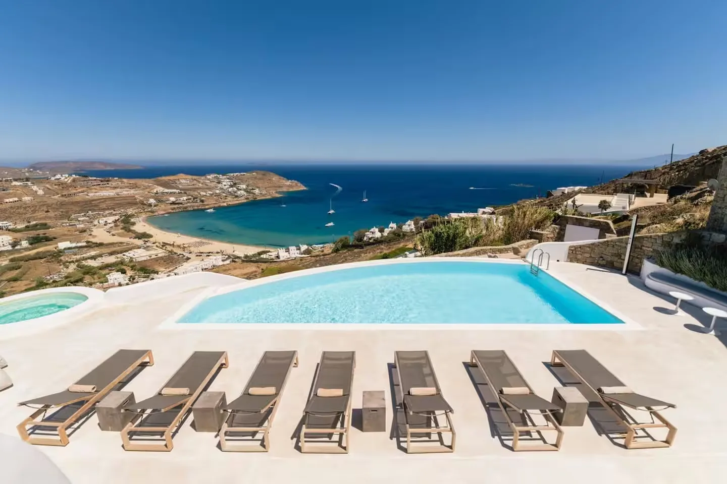 A swimming pool overlooks a coastal bay, with loungers arranged on the terrace.