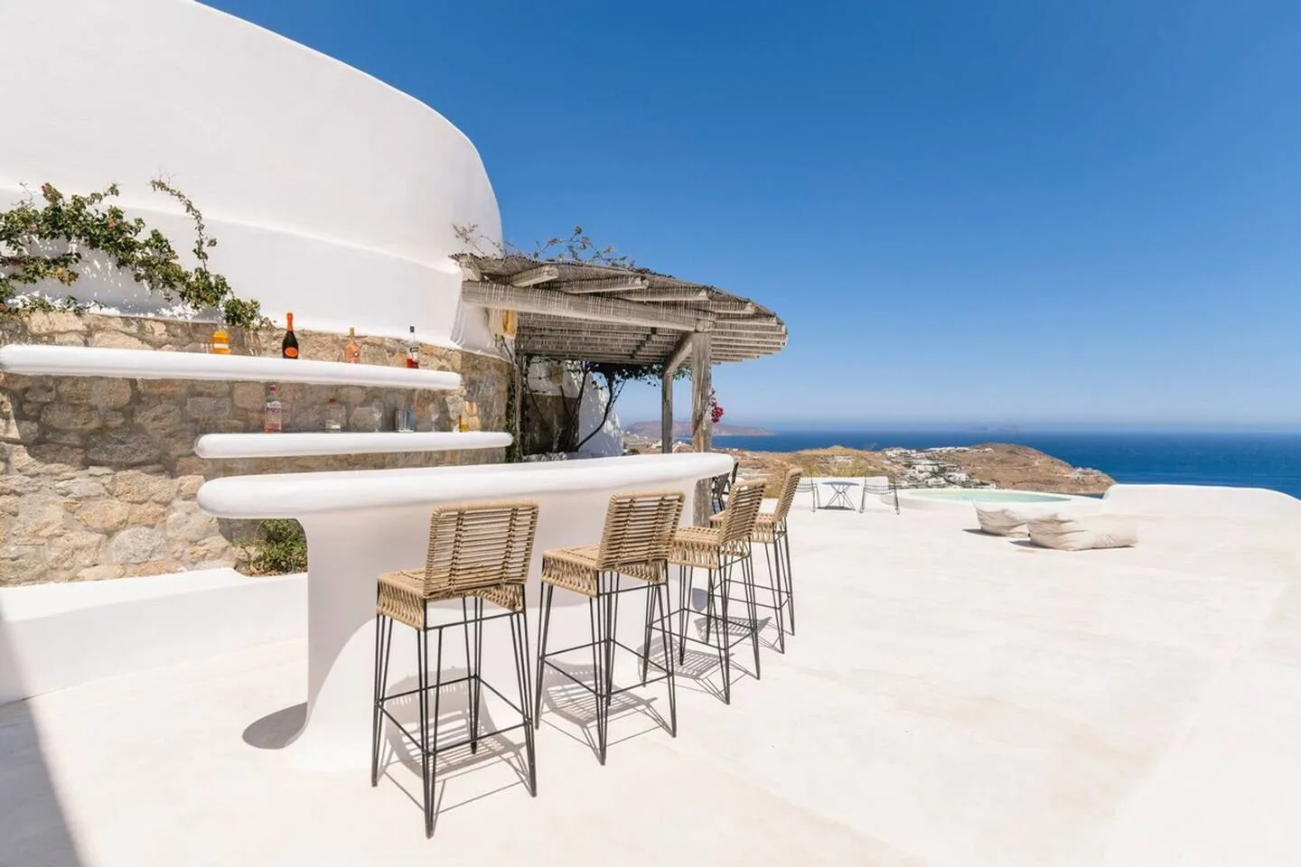 A bright outdoor terrace has a curved bar with woven seating and a sea view.