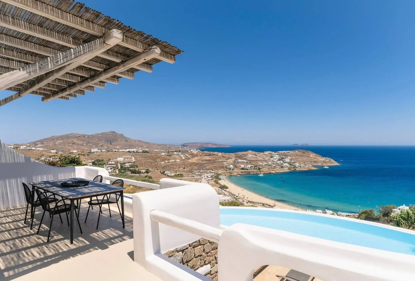 An outdoor dining area overlooks a swimming pool and the coastline.