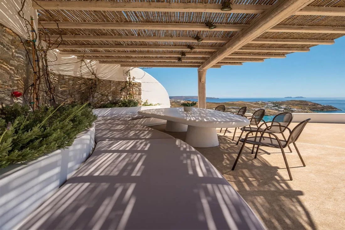 A shaded outdoor dining area with a table and seating overlooking the sea.