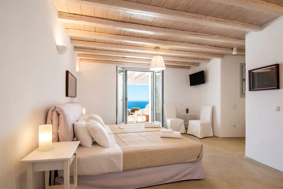 A bedroom with a bed facing open doors and a view of the sea.
