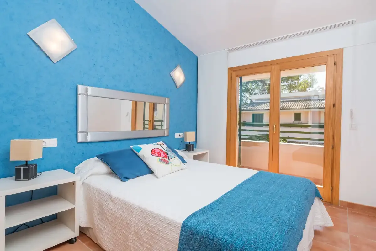 Un dormitorio con una cama junto a una pared azul y una puerta acristalada al balcón.