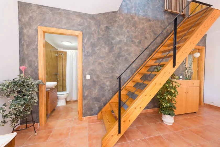 Un pasillo interior con una escalera de madera y la entrada de un baño.