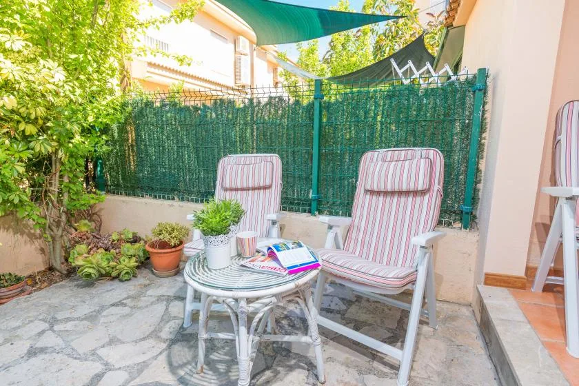 Un patio exterior con asientos a rayas, una mesita y plantas en macetas.