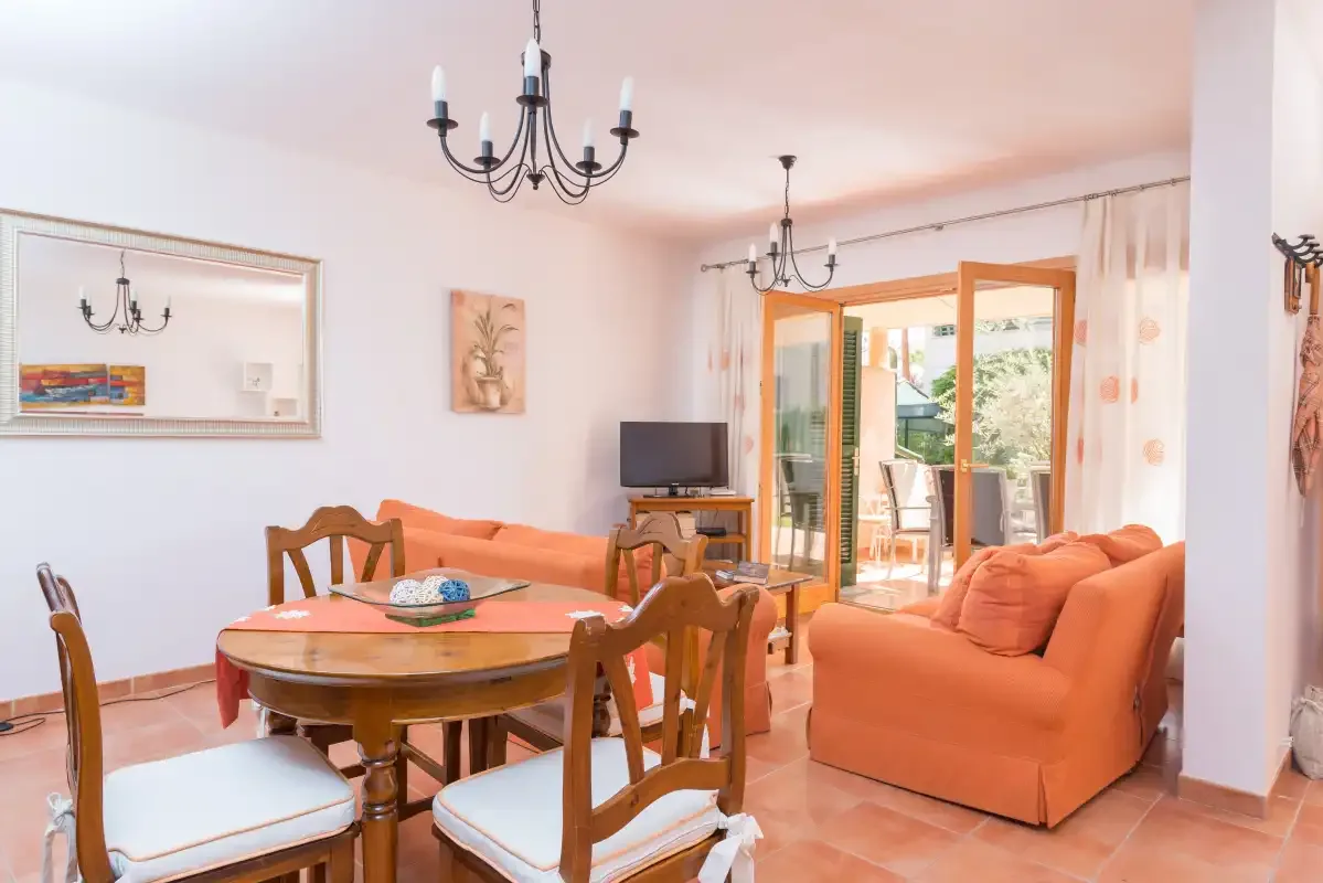 Sala de estar y comedor con asientos, una mesa y puertas abiertas a un patio.