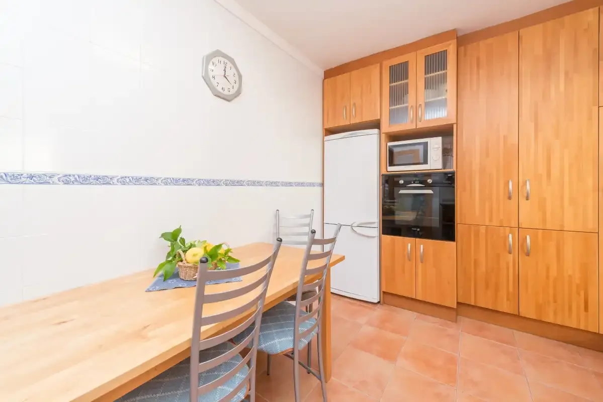 Una cocina con suelo de baldosas, armarios de madera, electrodomésticos integrados y una mesa.