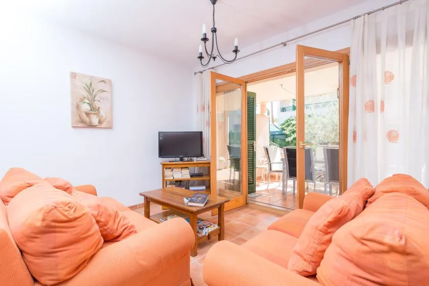 Una sala de estar con asientos naranjas, un televisor y puertas abiertas a un patio.