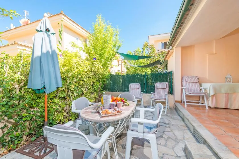 Un patio soleado con asientos y una mesa bajo una cubierta de sombra.