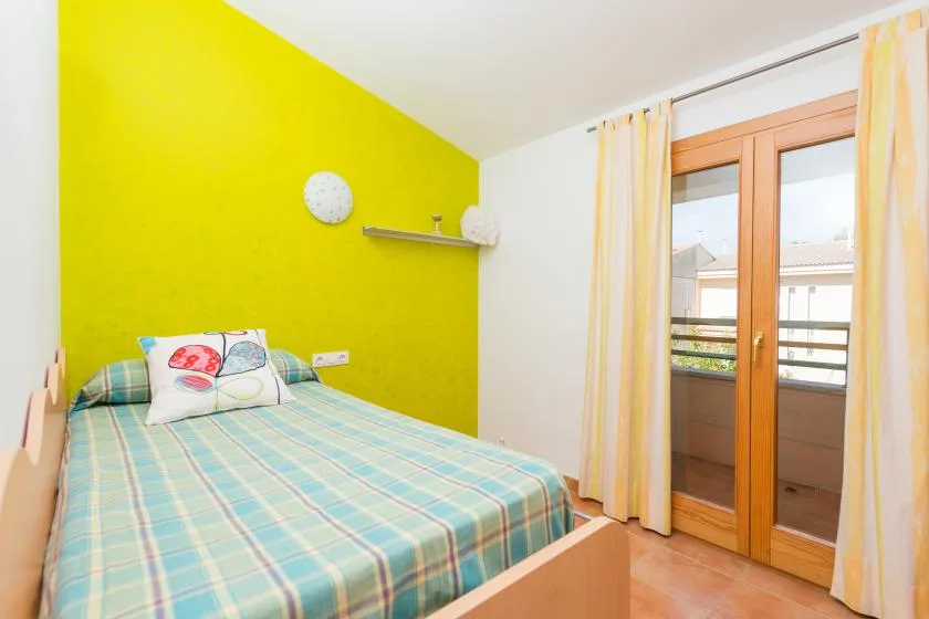 Un dormitorio con una colcha a cuadros y una puerta de vidrio que da a un balcón.