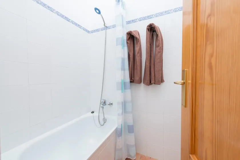 Un baño de azulejos con bañera, ducha y toallas colgadas.