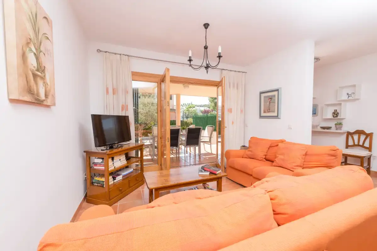Una sala de estar con asientos naranjas, un televisor y puertas abiertas a un patio.