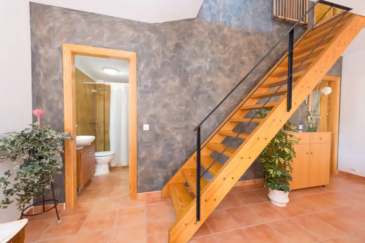 Un pasillo interior con una escalera de madera y la entrada a un baño.