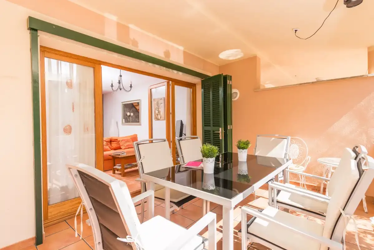 Un comedor con mesa de cristal y asientos se abre a una sala de estar.
