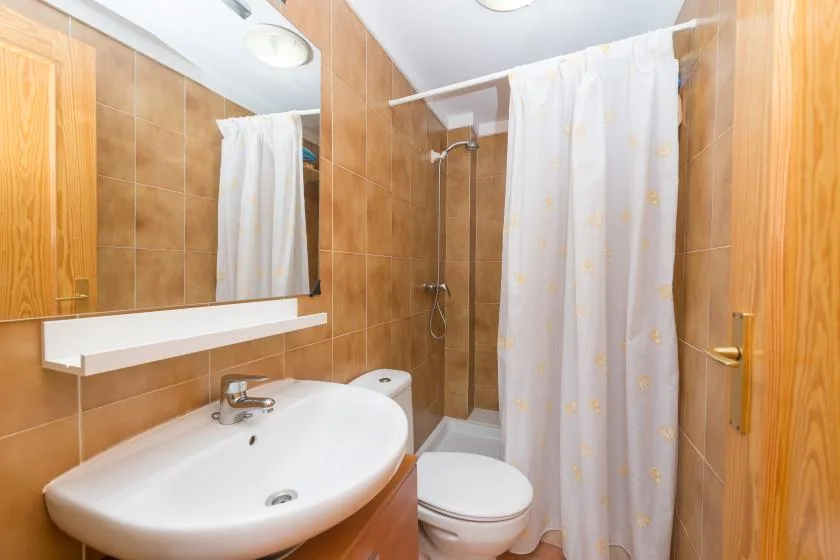 Un baño alicatado con lavabo, inodoro y ducha con cortina.