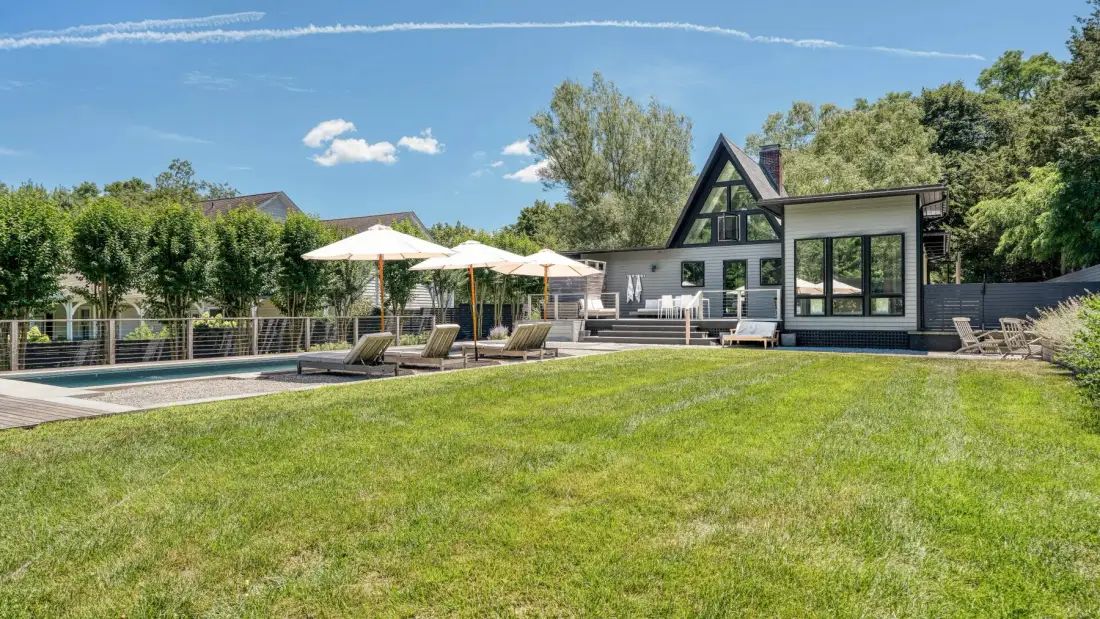 Una casa moderna da a un césped cuidado, una zona de descanso en el patio y una piscina.