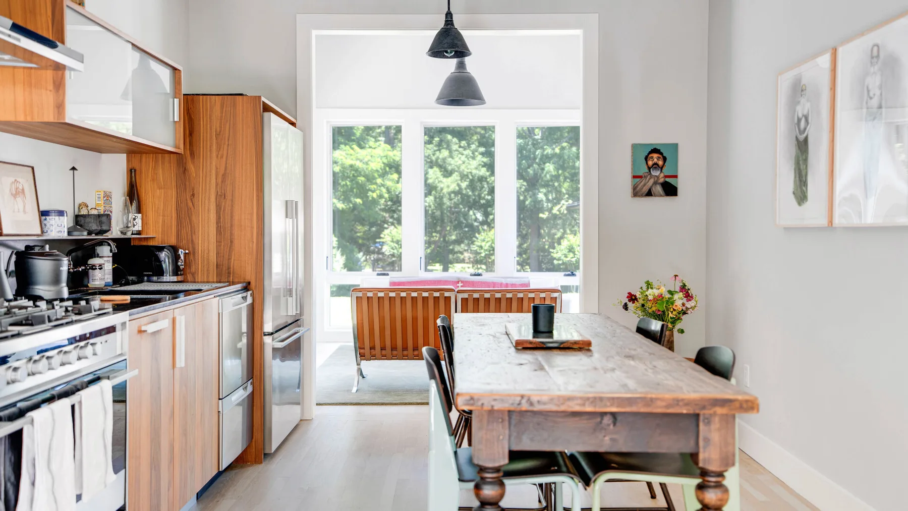 Una cocina luminosa con comedor tiene gabinetes de madera, una mesa larga y grandes ventanas.
