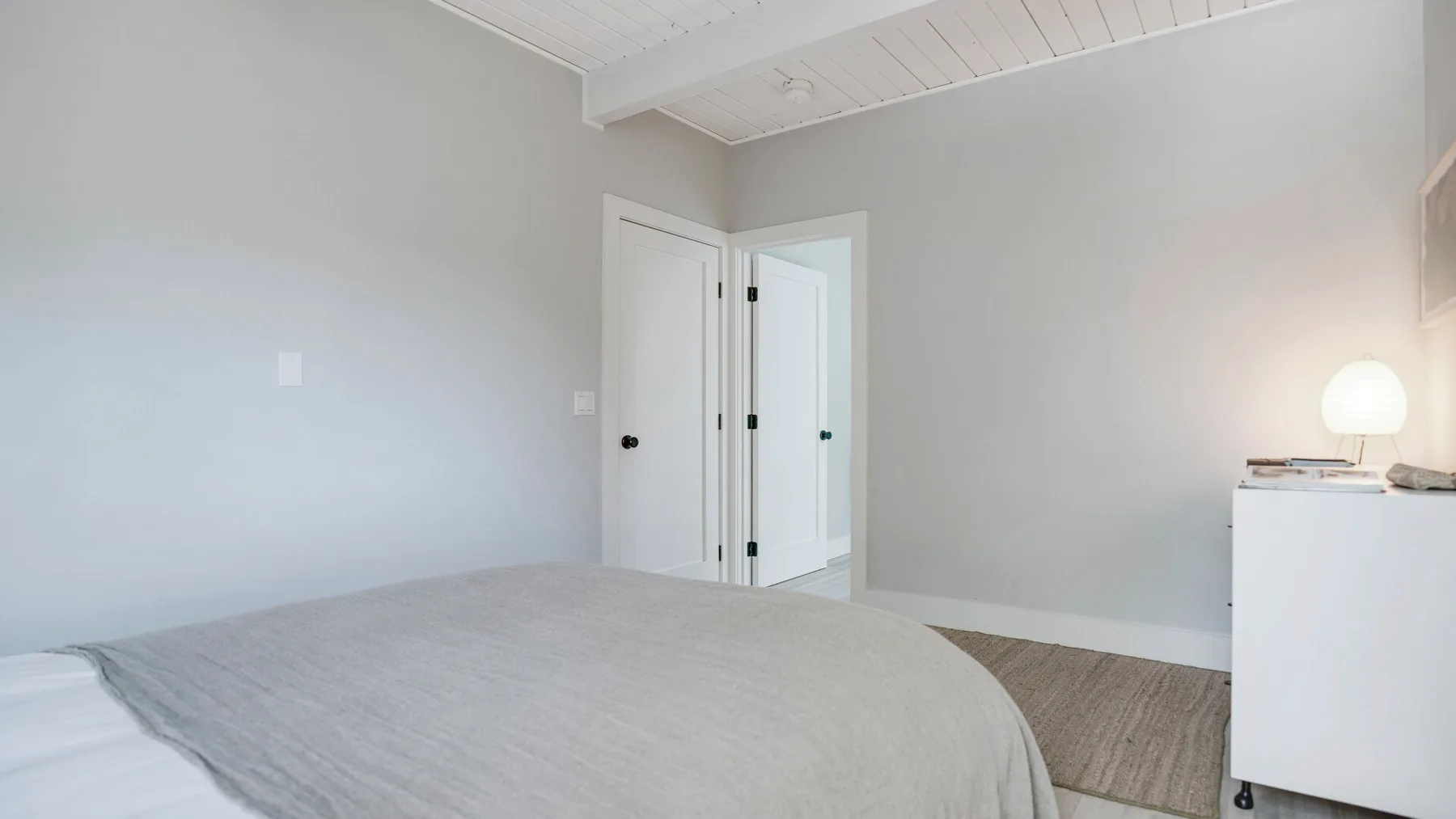 Un dormitorio con una cama, una cómoda blanca y una puerta abierta.