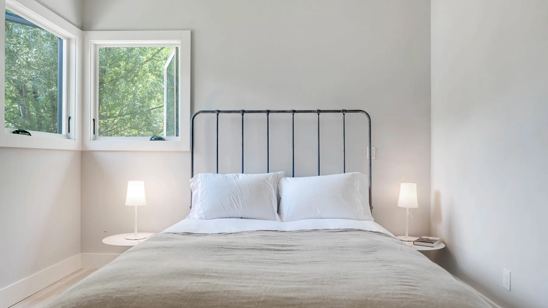Un dormitorio con una cama tendida bajo dos ventanas.