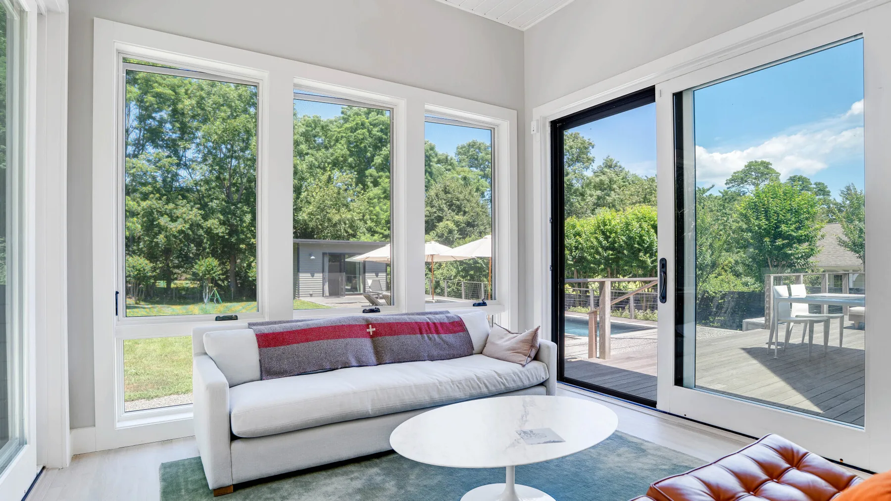 Una sala luminosa con sofá, mesa redonda y grandes ventanas con vistas a una terraza.