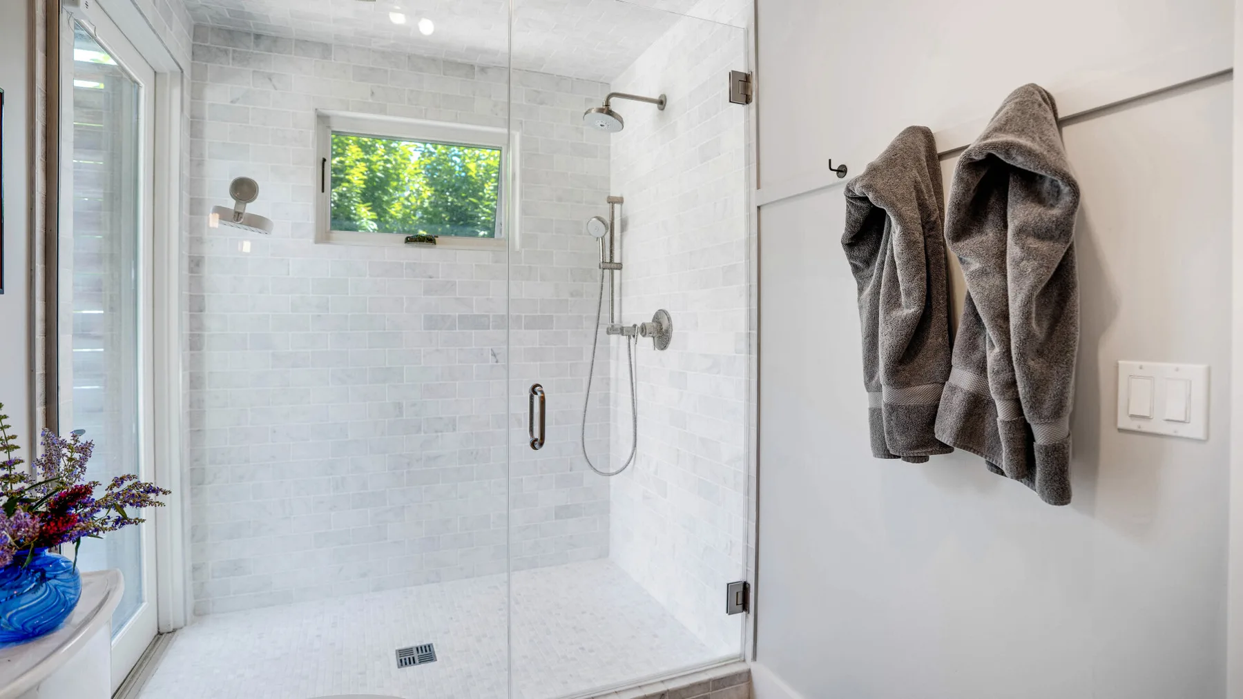 Un baño luminoso con ducha de vidrio y toallas colgadas en la pared.