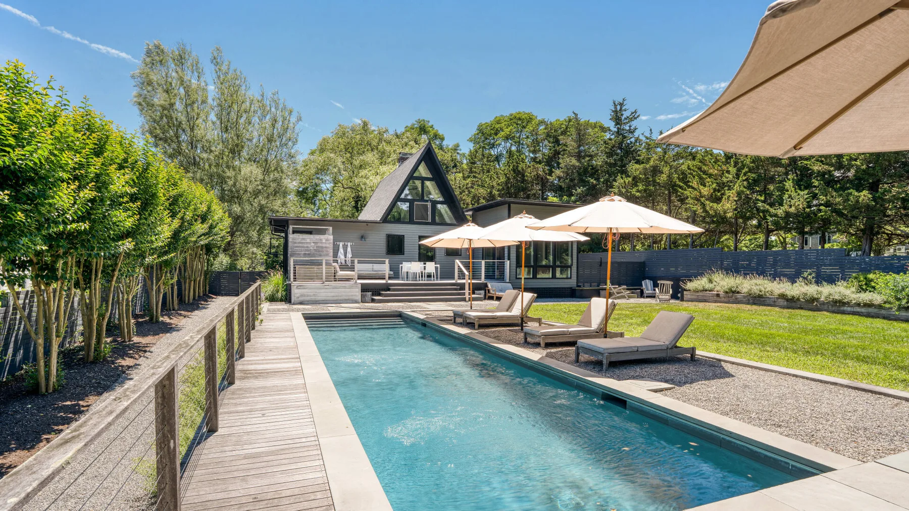 An outdoor swimming pool beside a wooden deck, with lounge seating and umbrellas.