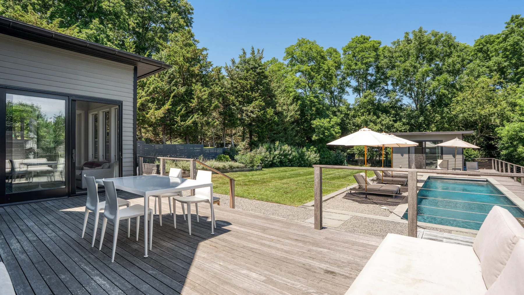 Una terraza soleada tiene una mesa de comedor, asientos y una piscina.