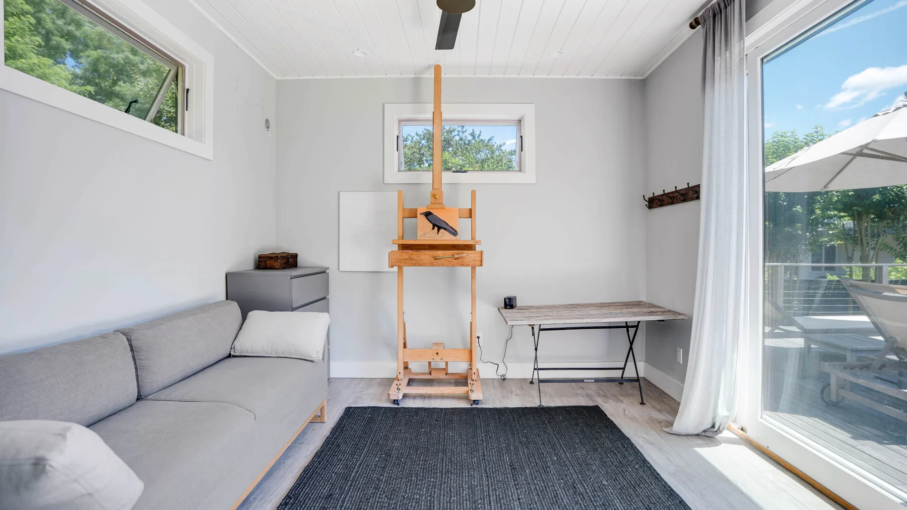 Una sala luminosa con asientos, una mesa pequeña y puertas de vidrio hacia un patio.