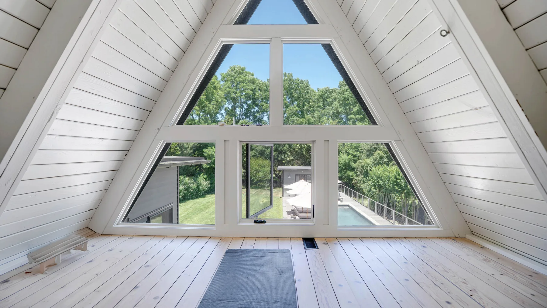 Una luminosa habitación abuhardillada con una gran ventana triangular frente a árboles verdes.