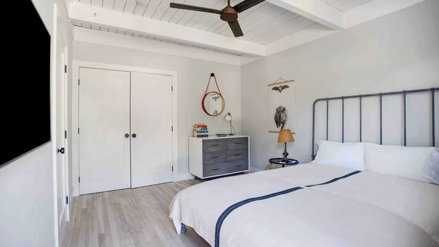 Un dormitorio luminoso con cama blanca, cabecero oscuro y ventilador de techo.