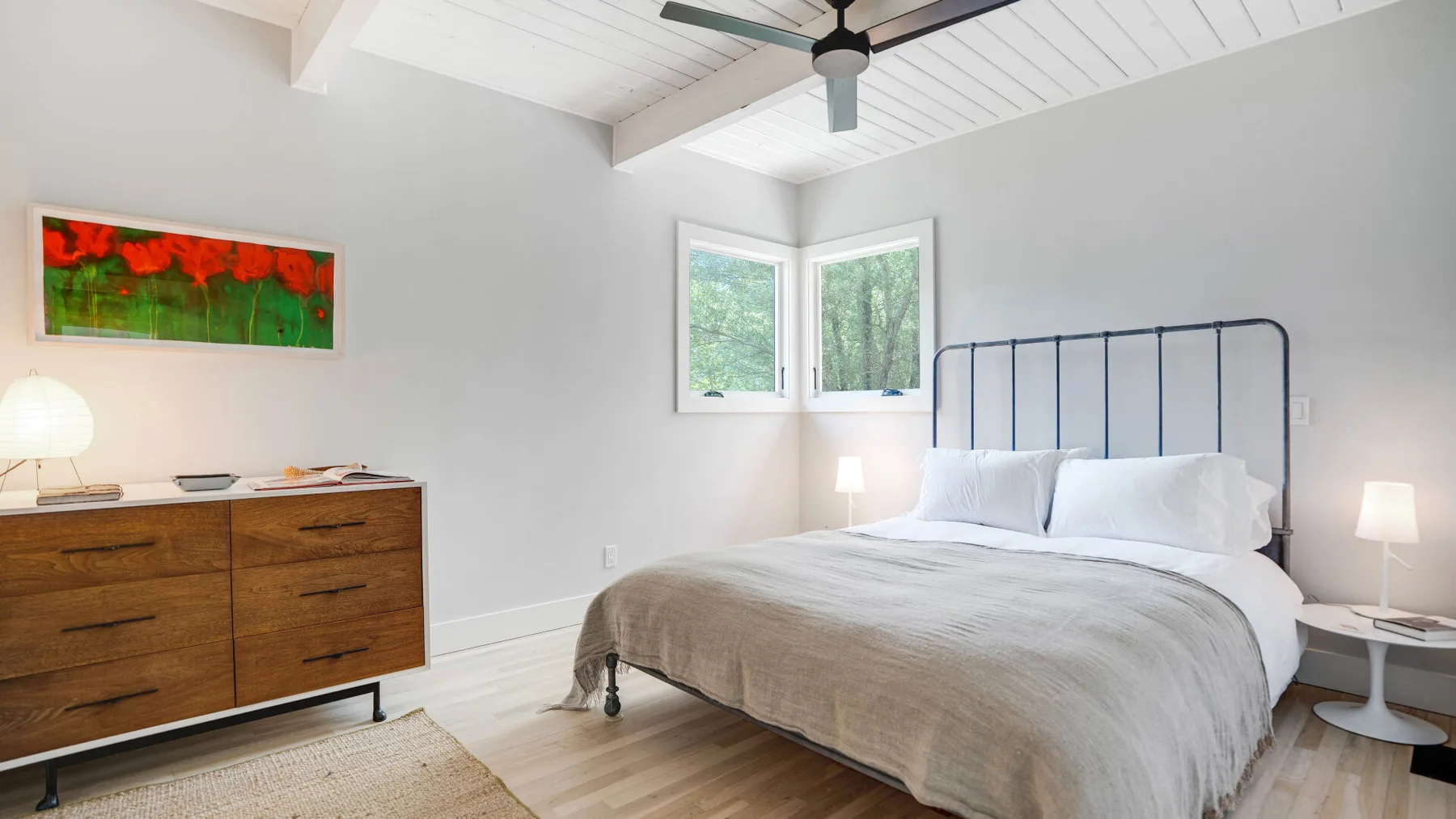 Un dormitorio luminoso con una cama, una cómoda de madera y ventanas.