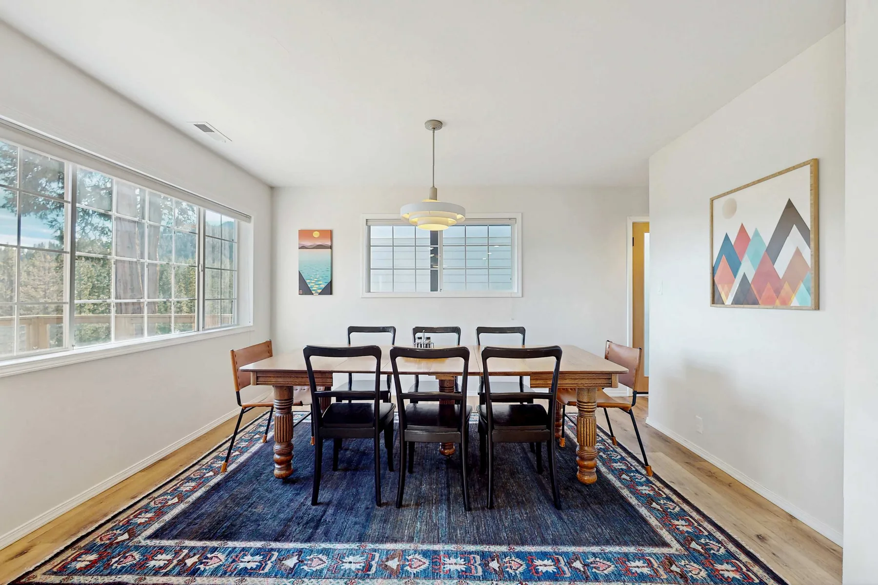 A dining room with a wooden table and chairs on a patterned rug.