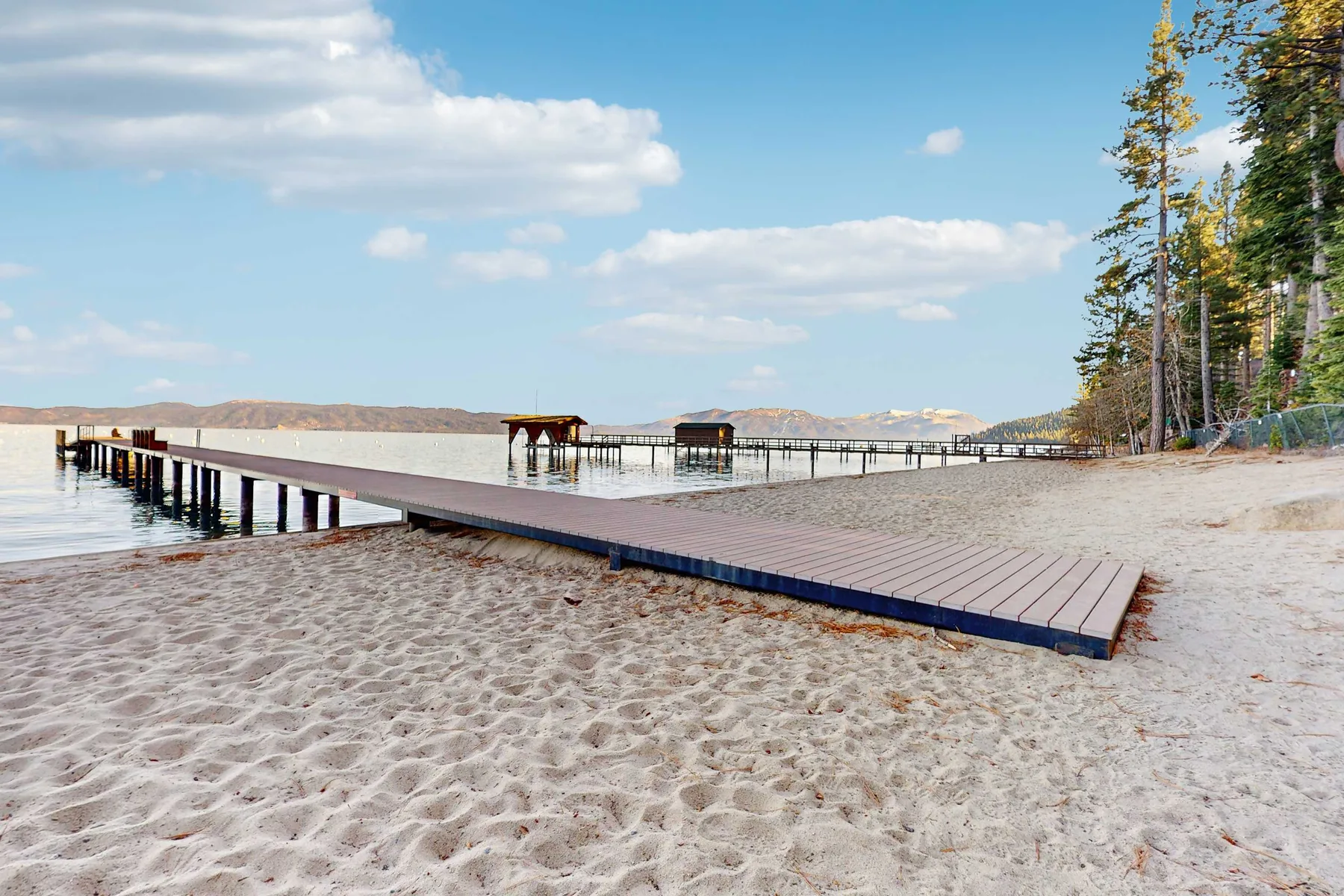 A long wooden pier extends from a sandy beach over the water.