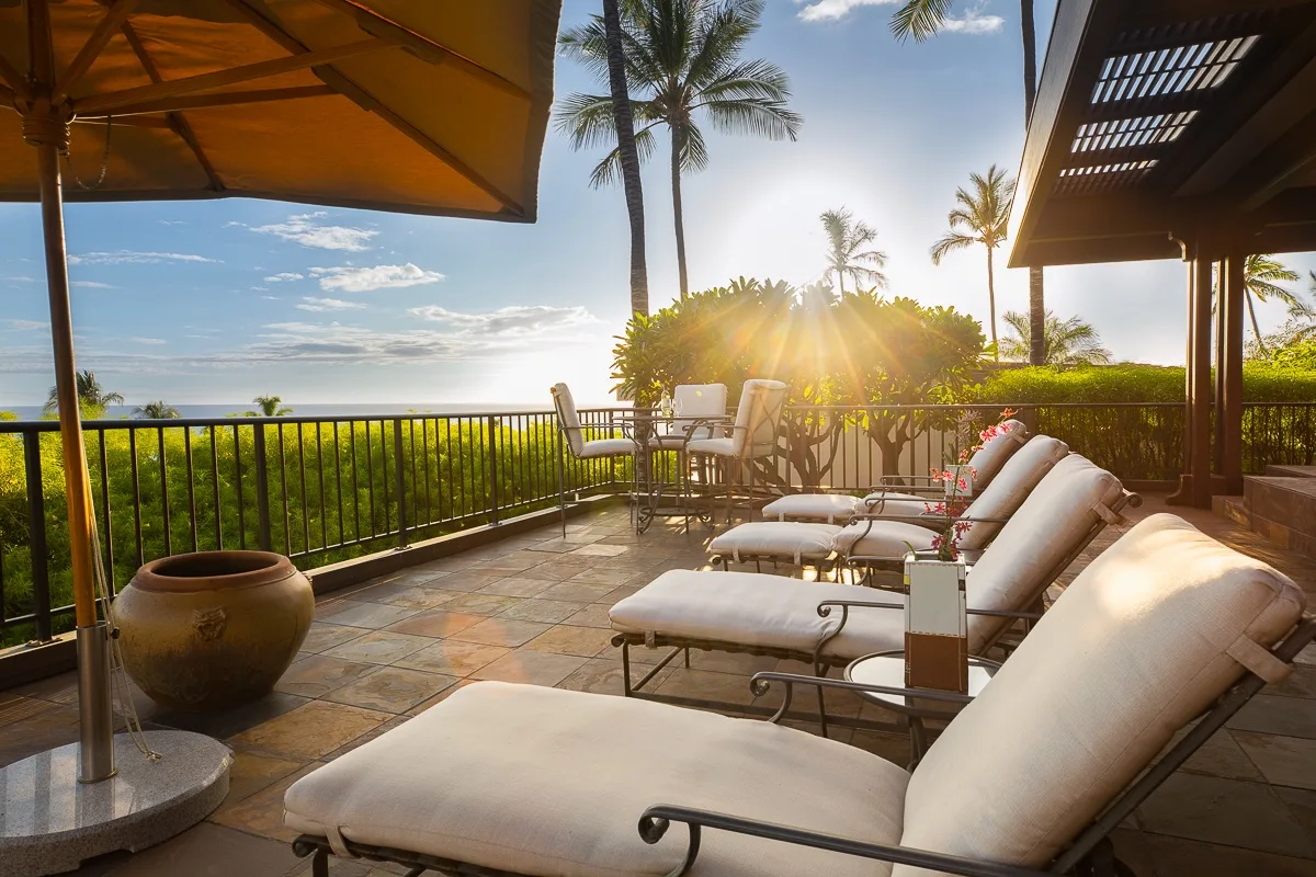 A sunny outdoor patio with cushioned loungers, a dining table, and tropical plants.