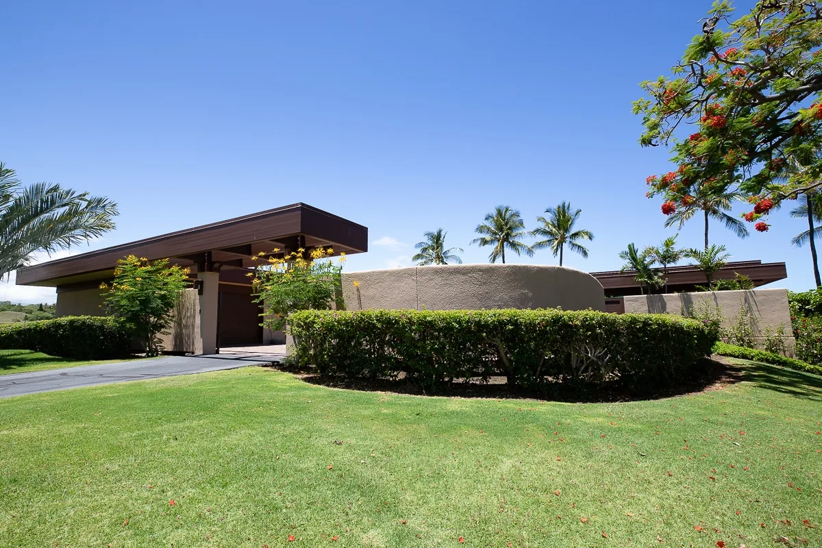 A low modern building stands behind trimmed hedges and a green lawn.