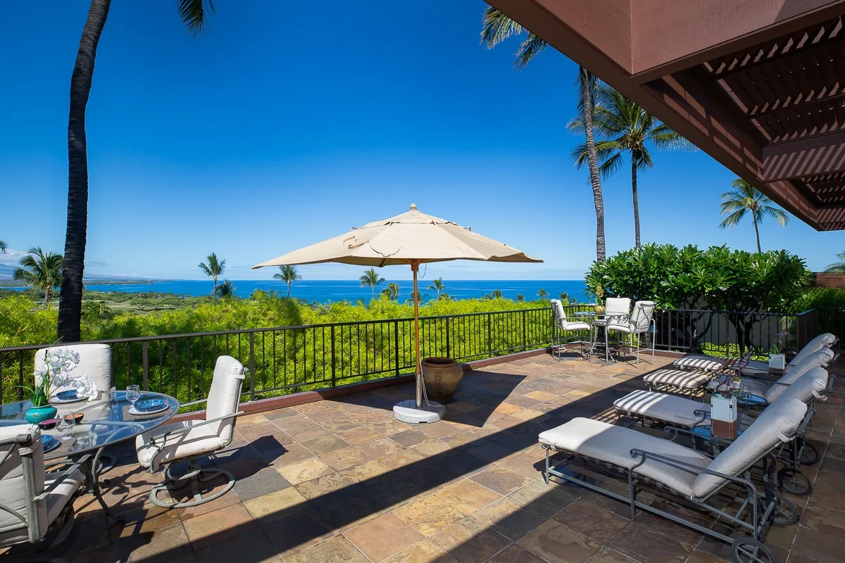 A seaside patio has lounge seating, a dining table, and a large sun umbrella.