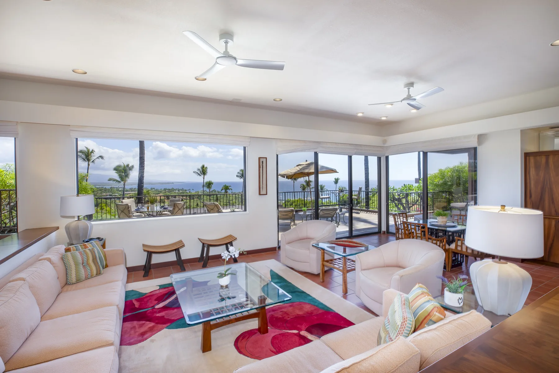 A bright living room with pale seating, a glass coffee table, and wide windows.