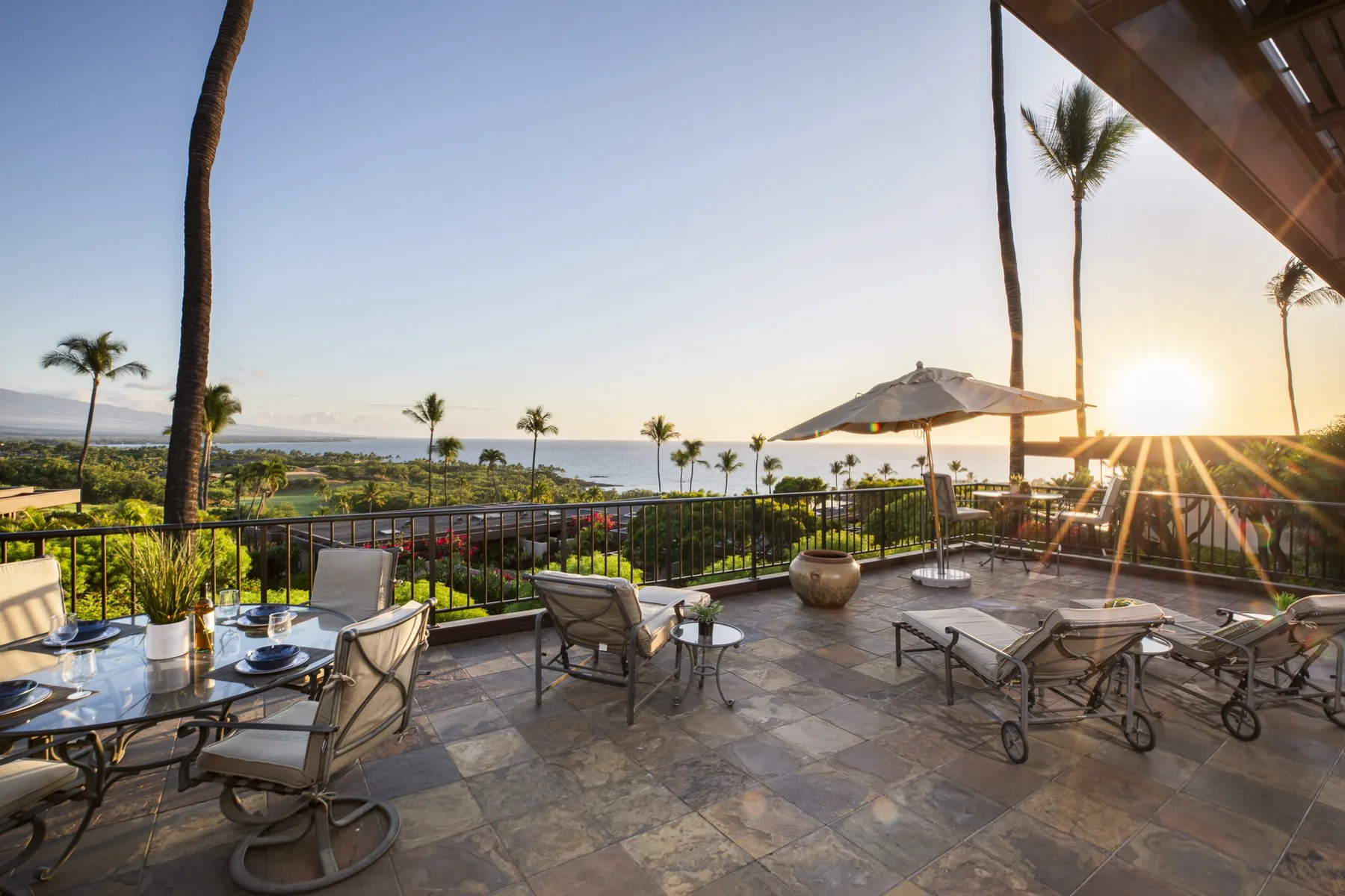 A furnished patio overlooks a coastal landscape at sunset.