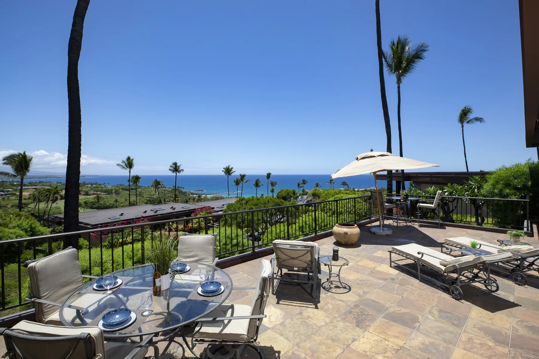 An outdoor terrace overlooks the ocean, with patio seating and an open umbrella.