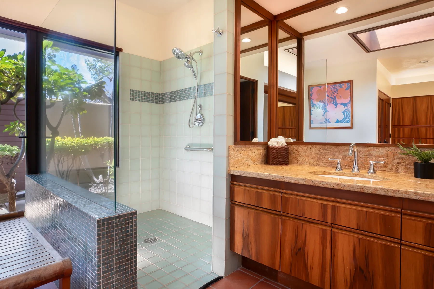 A bathroom with a glass shower beside a wood vanity and wide mirror.