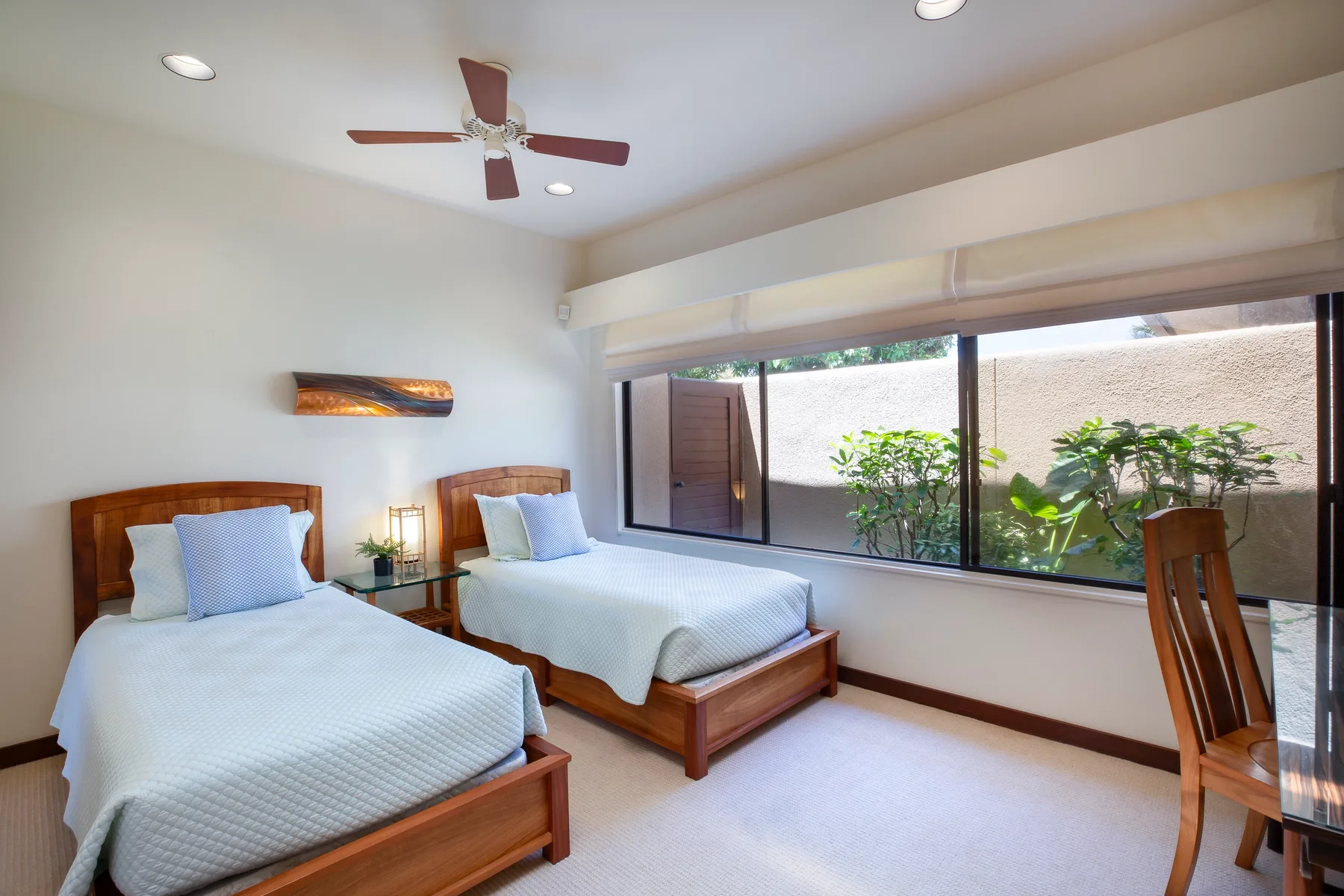 A bright bedroom with two beds beside a wide window overlooking greenery.