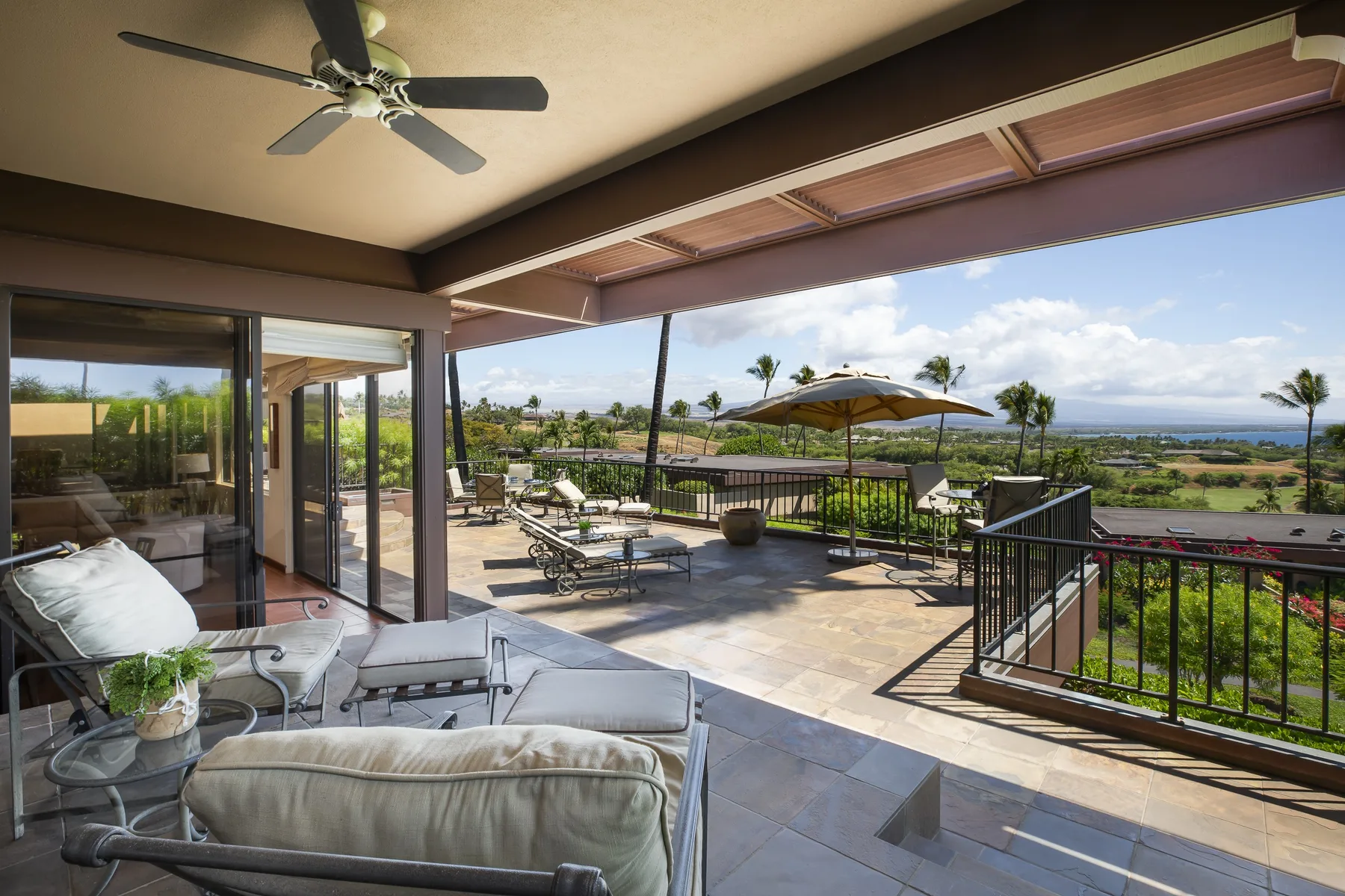 A covered patio with outdoor seating overlooks a landscaped garden and distant coastline.