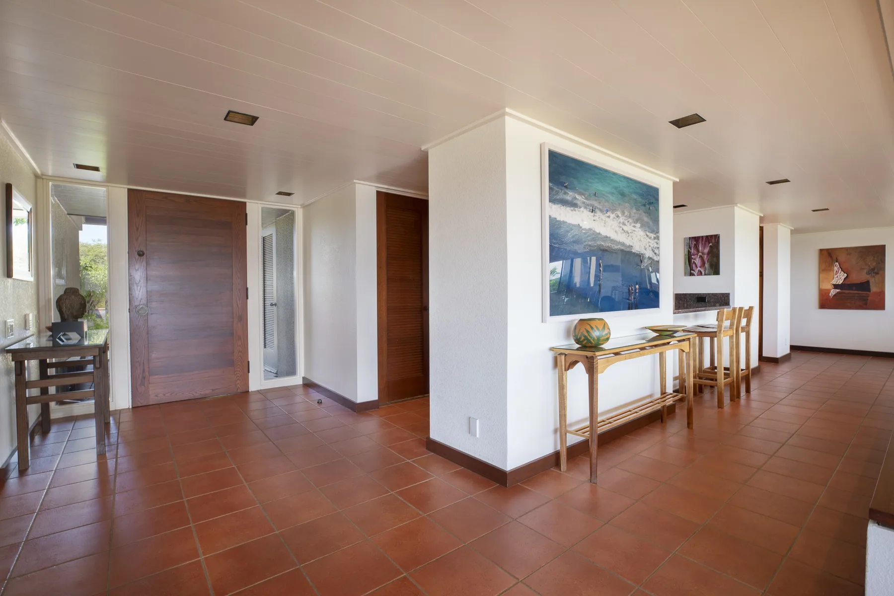 A bright interior hallway with terracotta-colored tile flooring and artwork on the walls.