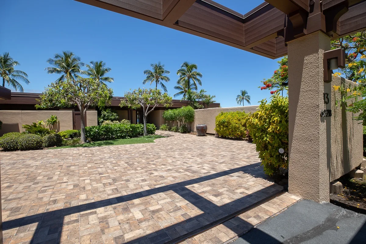 A paved courtyard with landscaped shrubs and palm trees beneath a covered entry.