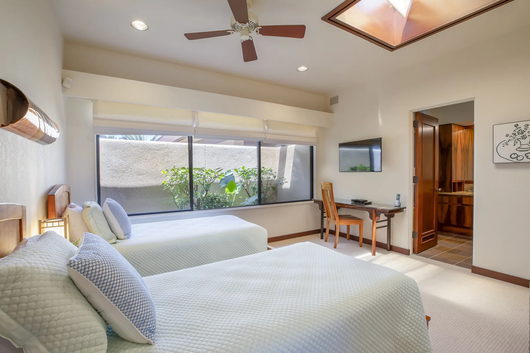 A bedroom with two beds beside a wide window and a small desk.