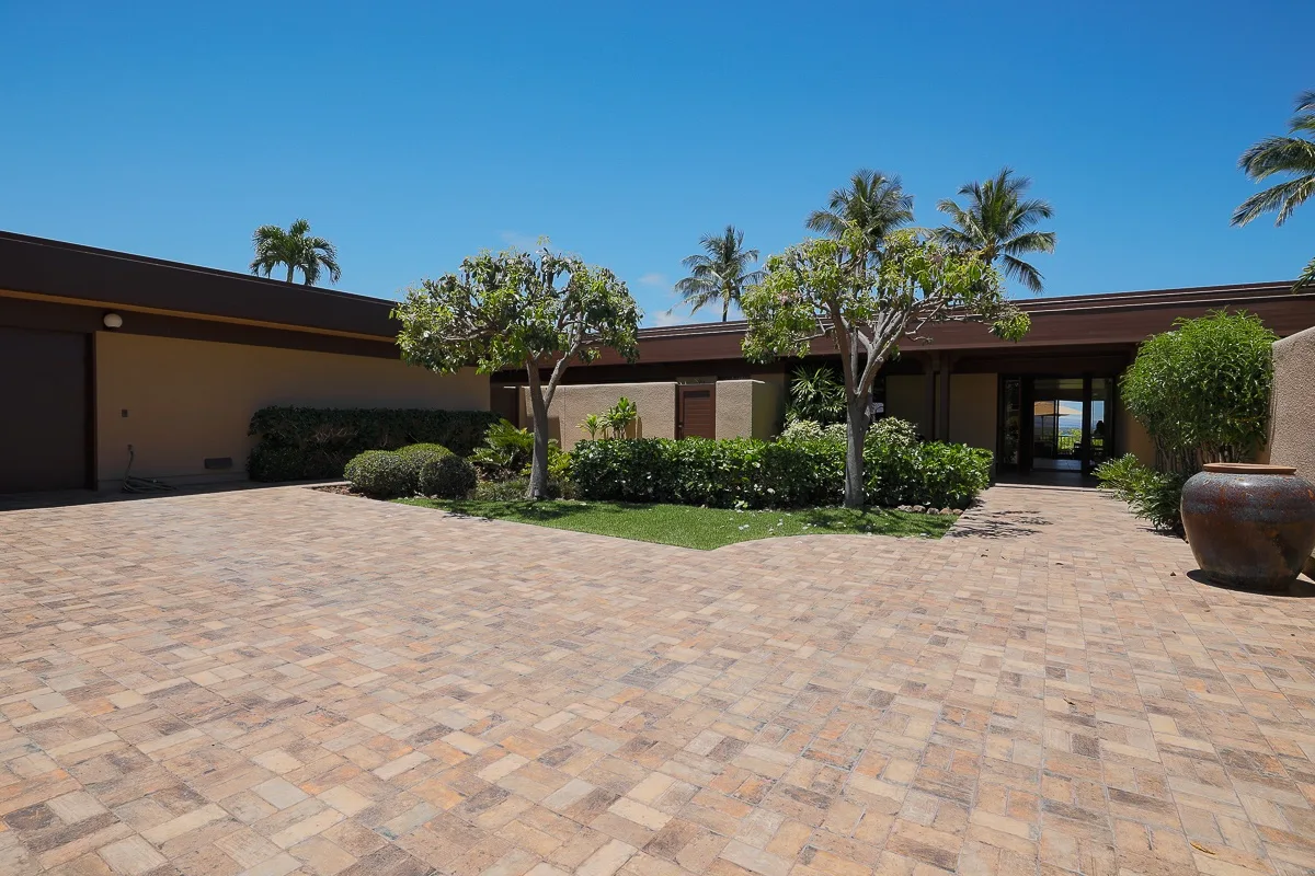 A low modern building borders a broad paved courtyard with palms and shrubs.