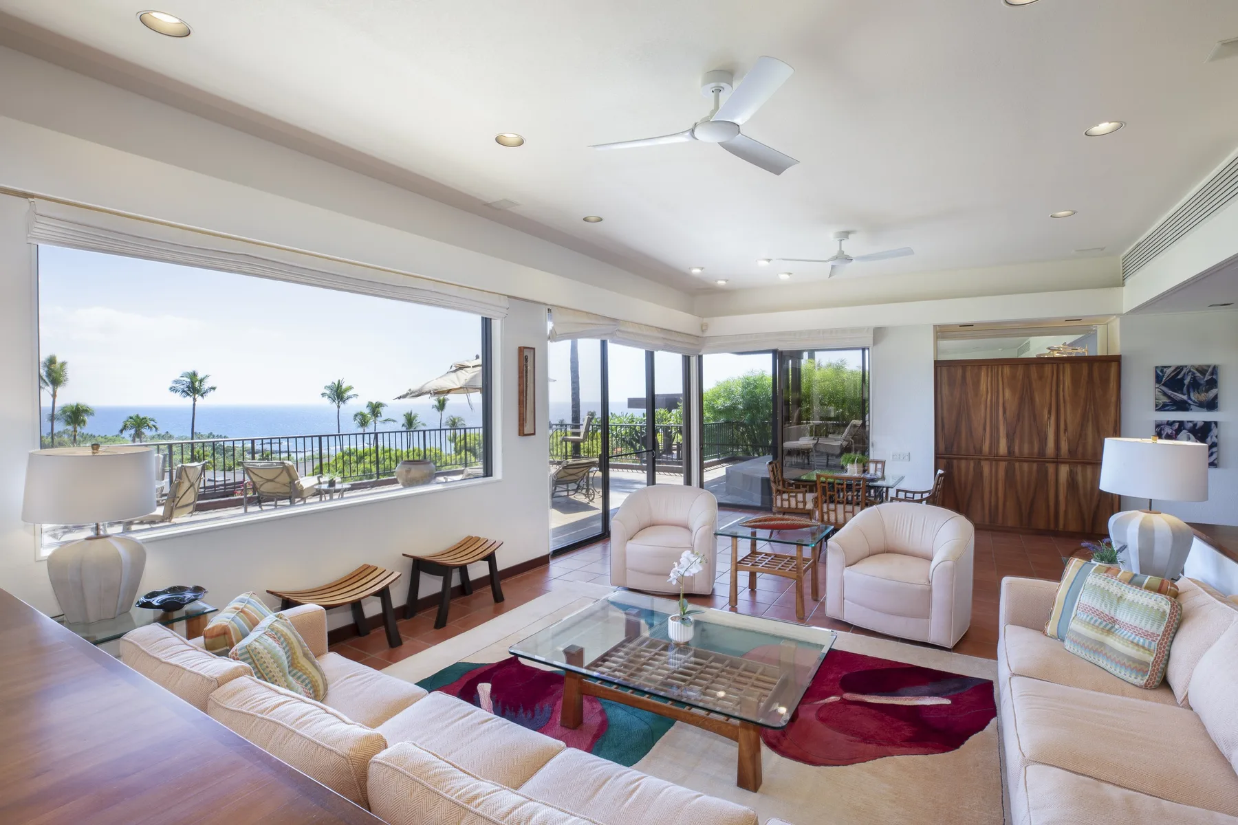 A bright living room opens onto a balcony with palm trees and ocean views.