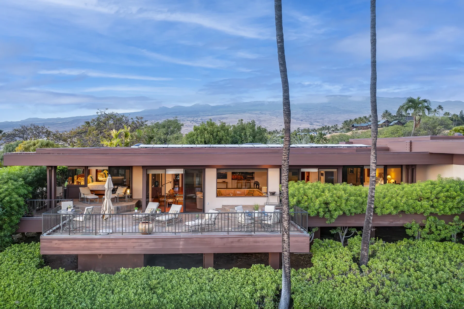 A modern home opens onto a broad terrace overlooking lush greenery and distant hills.